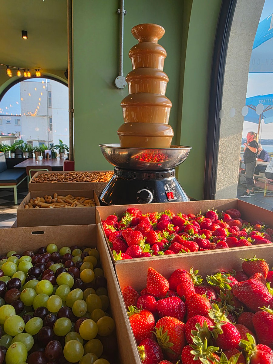 A tiered chocolate fountain with fresh strawberries, grapes, and other dipping treats ready for guests