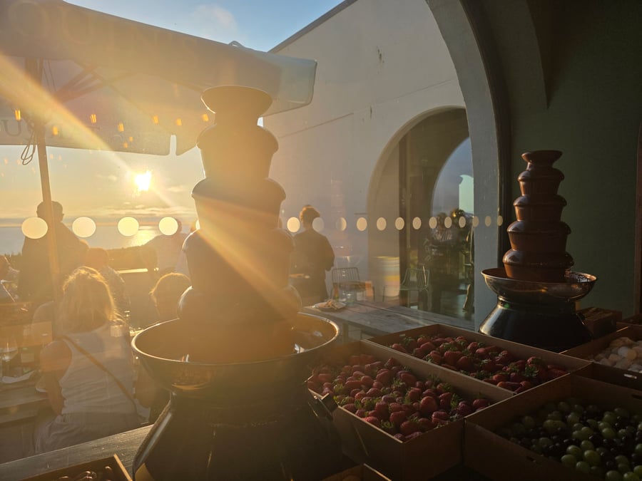 A chocolate fountain with fresh strawberries and grapes, set against a beautiful sunset over the sea (2)