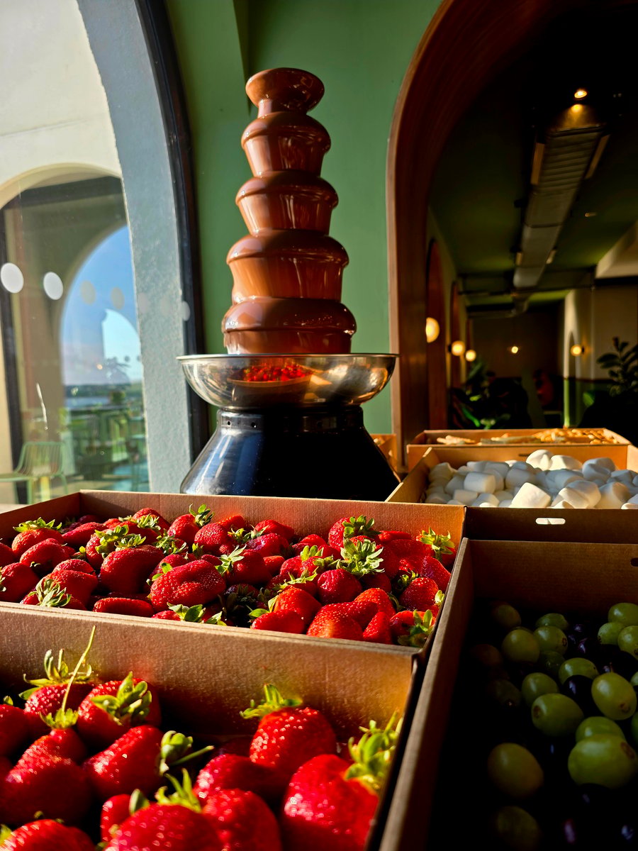 A tiered chocolate fountain with fresh strawberries, grapes, and marshmallows ready for dipping
