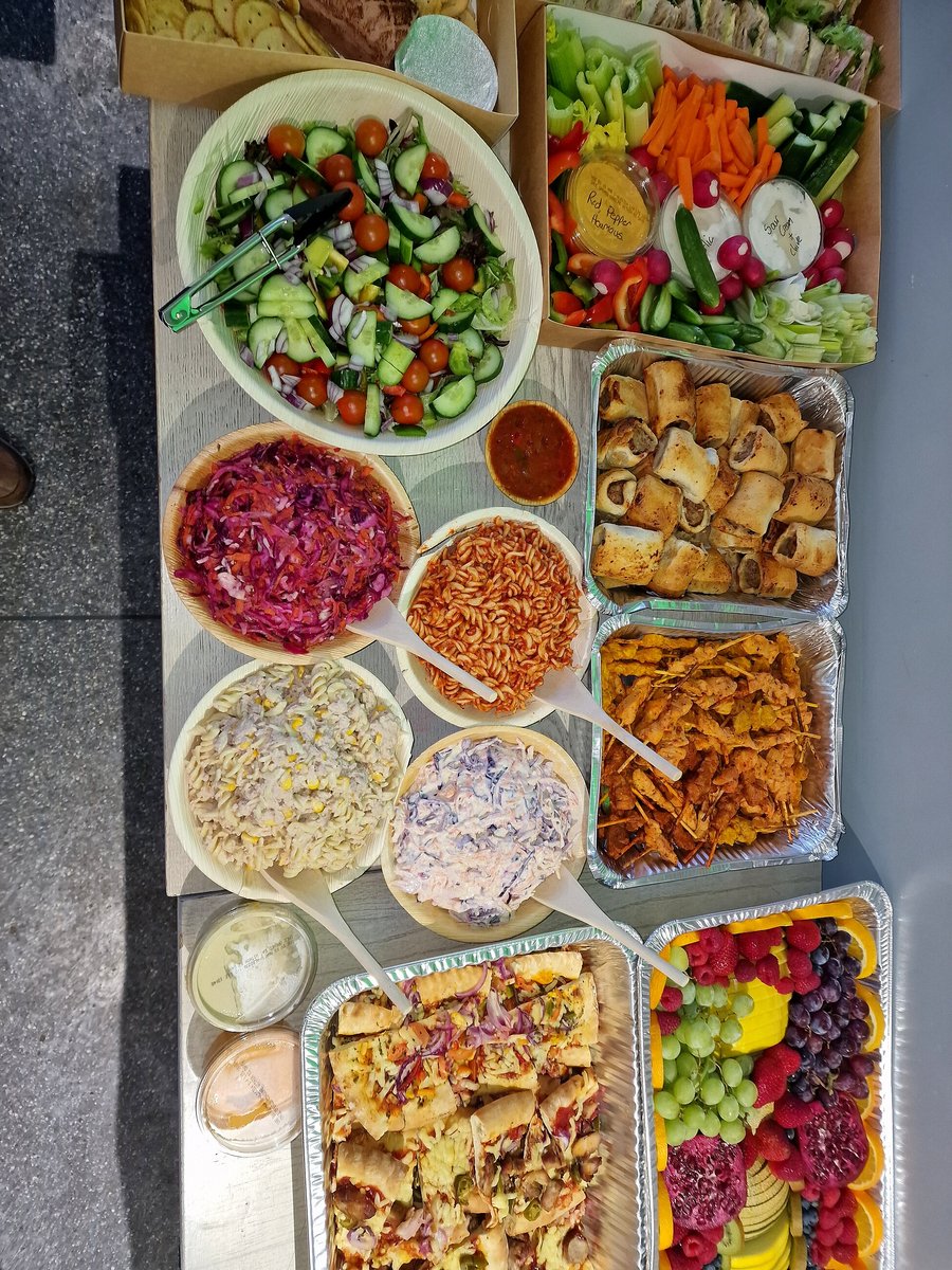 A diverse buffet spread featuring salads, pasta, pizza, sausage rolls, and fruit platter