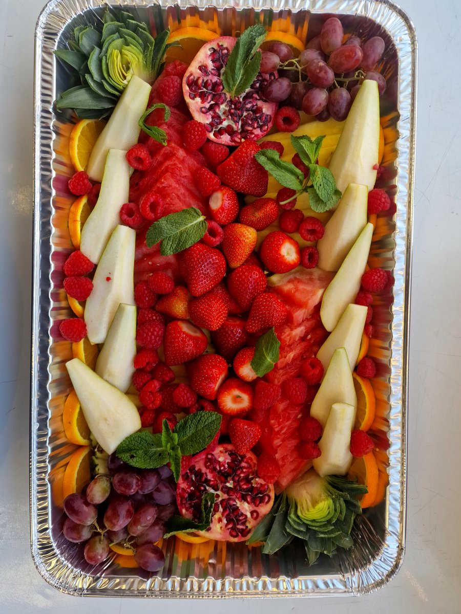 A large, foil catering tray filled with a vibrant assortment of fresh fruits
