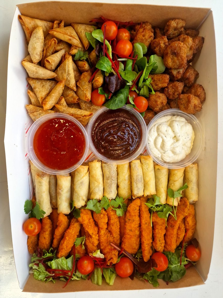 A catering box filled with samosas, spring rolls, chicken tenders, and dips