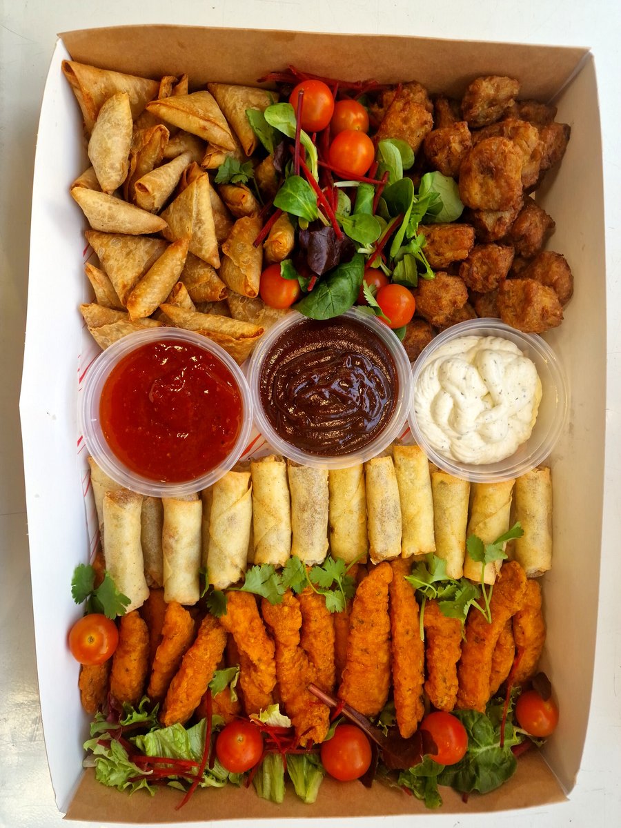 A catering box filled with samosas, spring rolls, chicken tenders, and dipping sauces