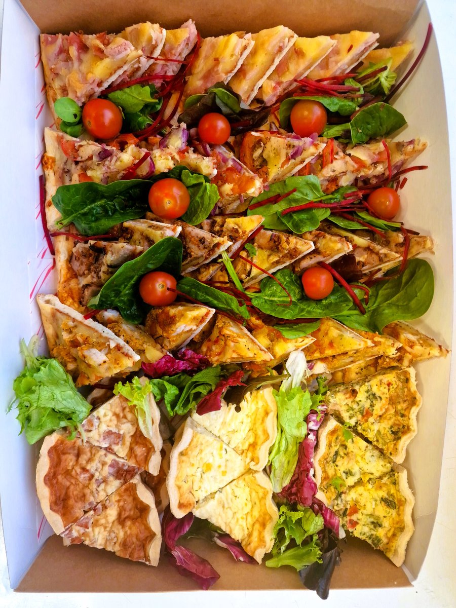 A catering box filled with assorted quiches, tarts, and fresh salad garnishes