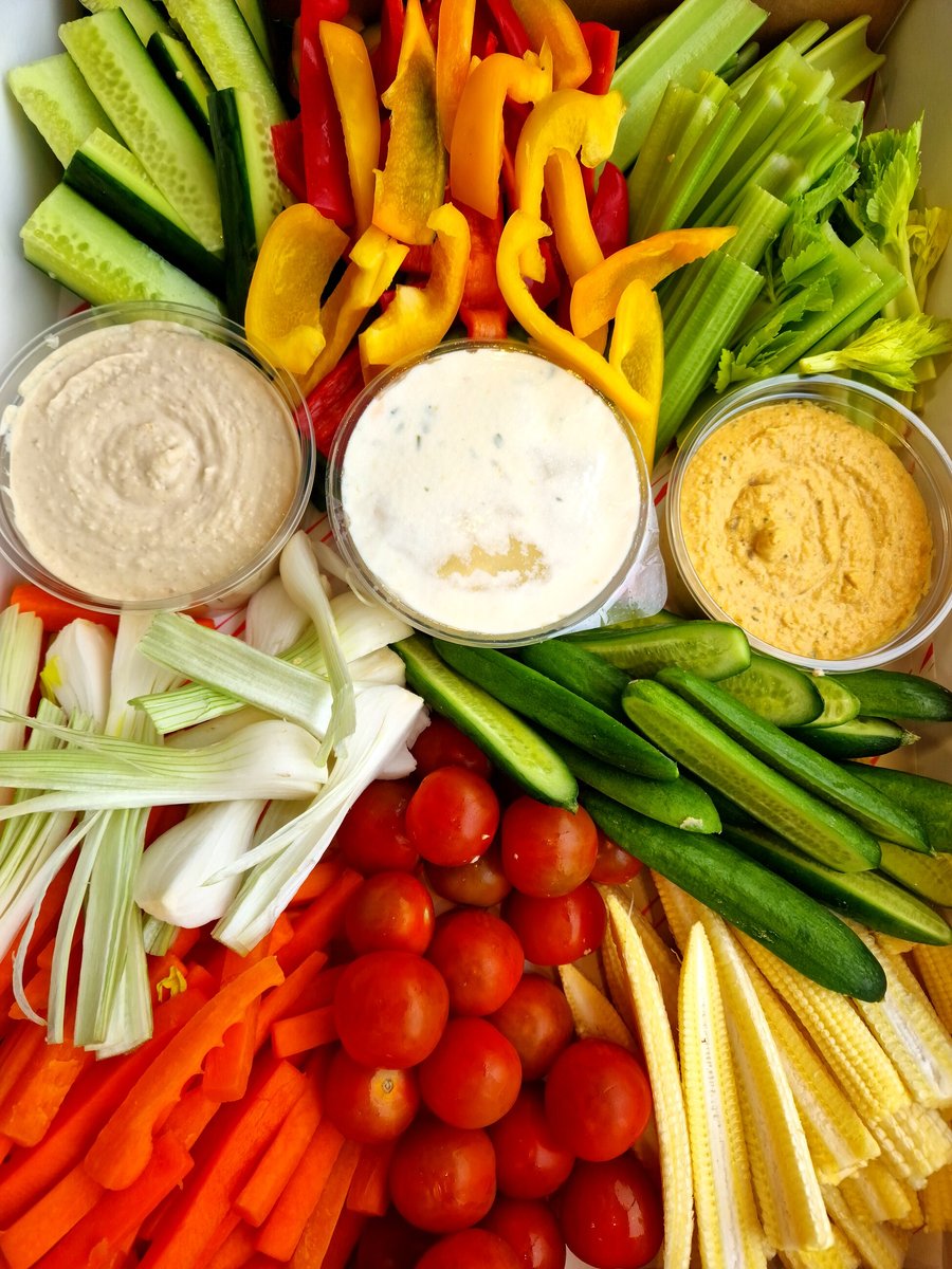 A platter of fresh crudités with three dips, including hummus and a creamy herb dip
