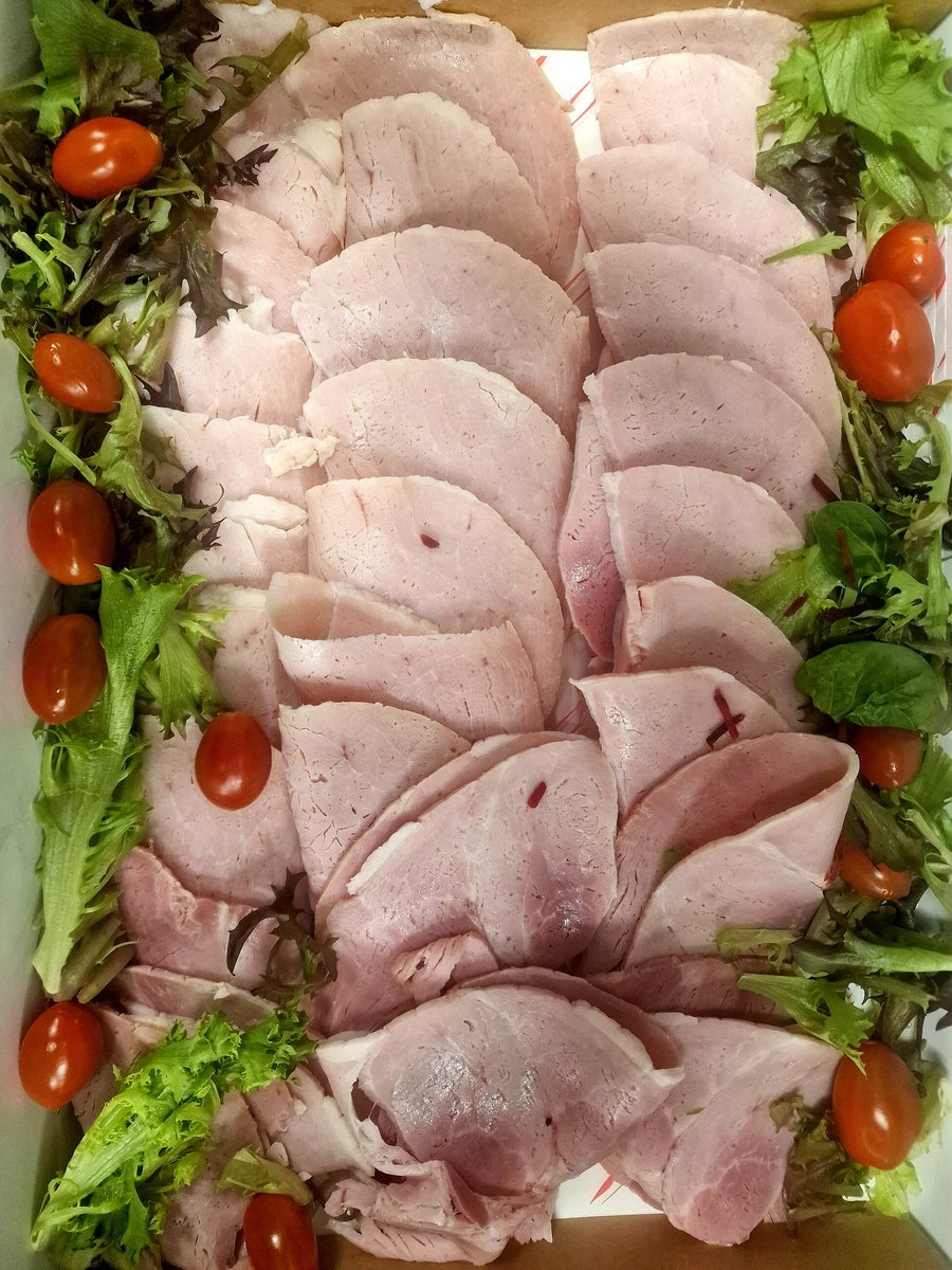 A platter of sliced ham garnished with cherry tomatoes and salad leaves