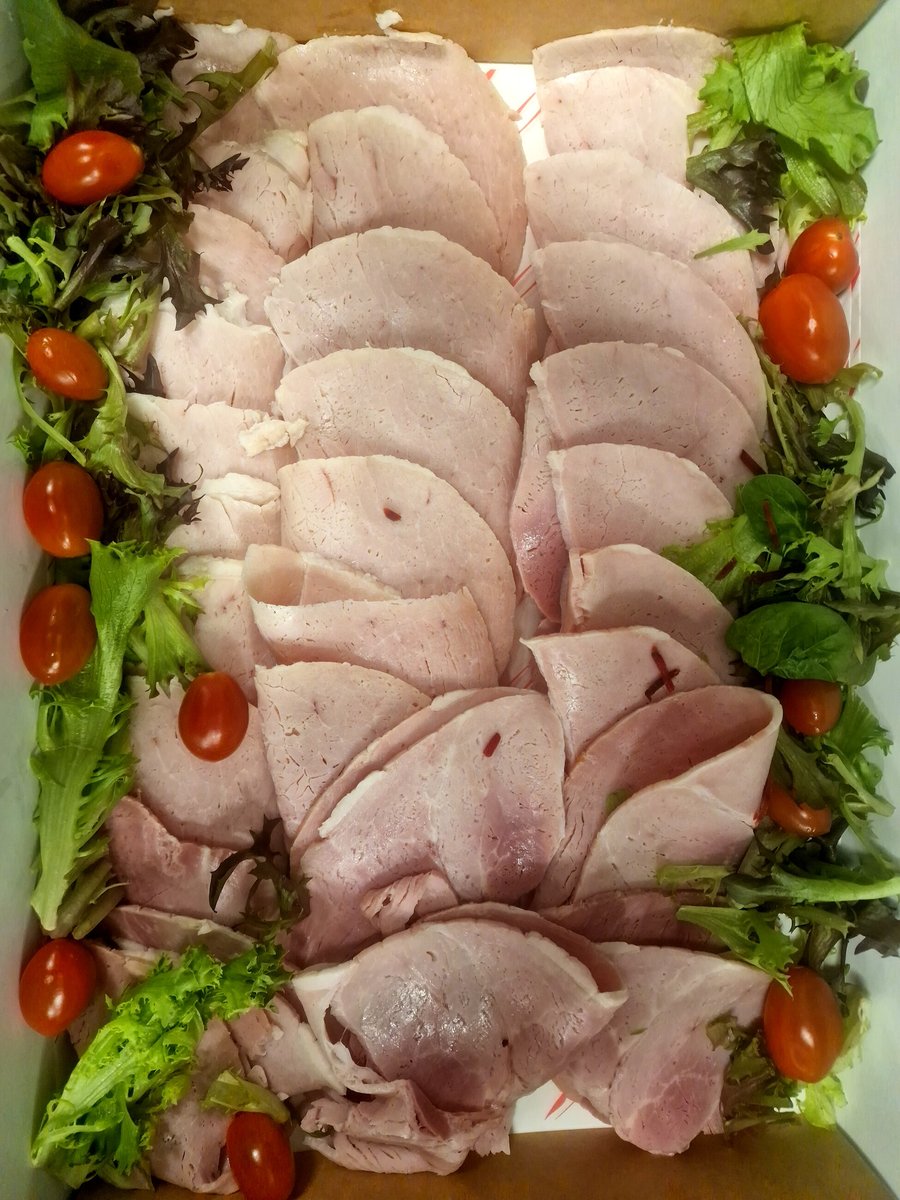 A platter of sliced ham, cherry tomatoes, and salad leaves in a box