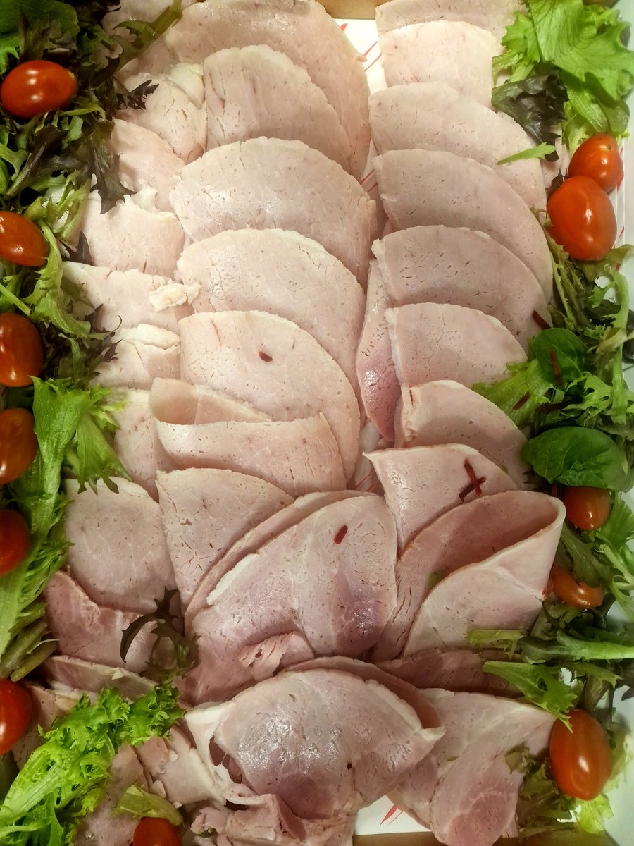 A platter of thinly sliced ham garnished with cherry tomatoes and lettuce