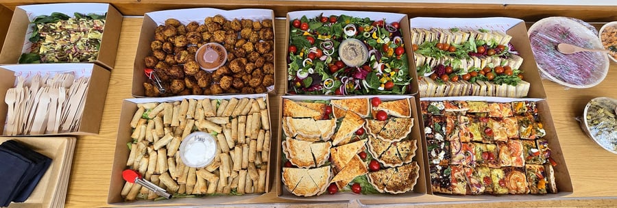 Assortment of catering boxes filled with sandwiches, quiches, salad, and finger foods