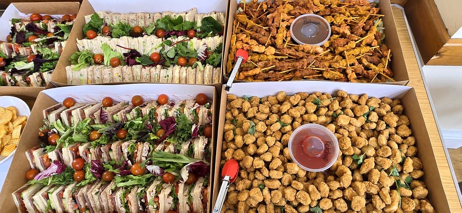 Assortment of catering boxes filled with sandwiches, skewers, and crispy bites