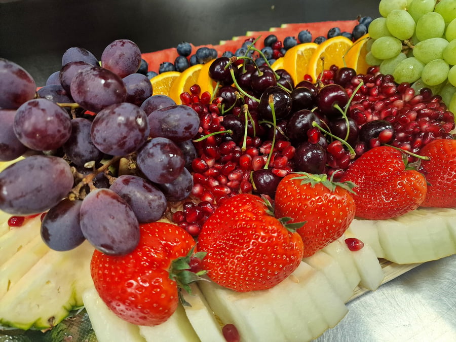 A vibrant and abundant fruit platter featuring strawberries, grapes, pomegranate, cherries, melon, and citrus