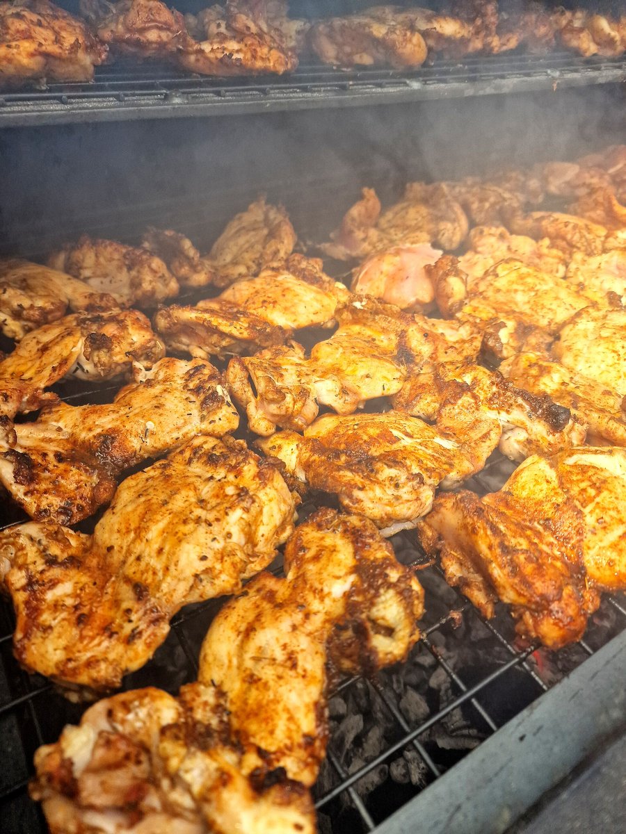 Chicken pieces are cooking on a grill with smoke rising