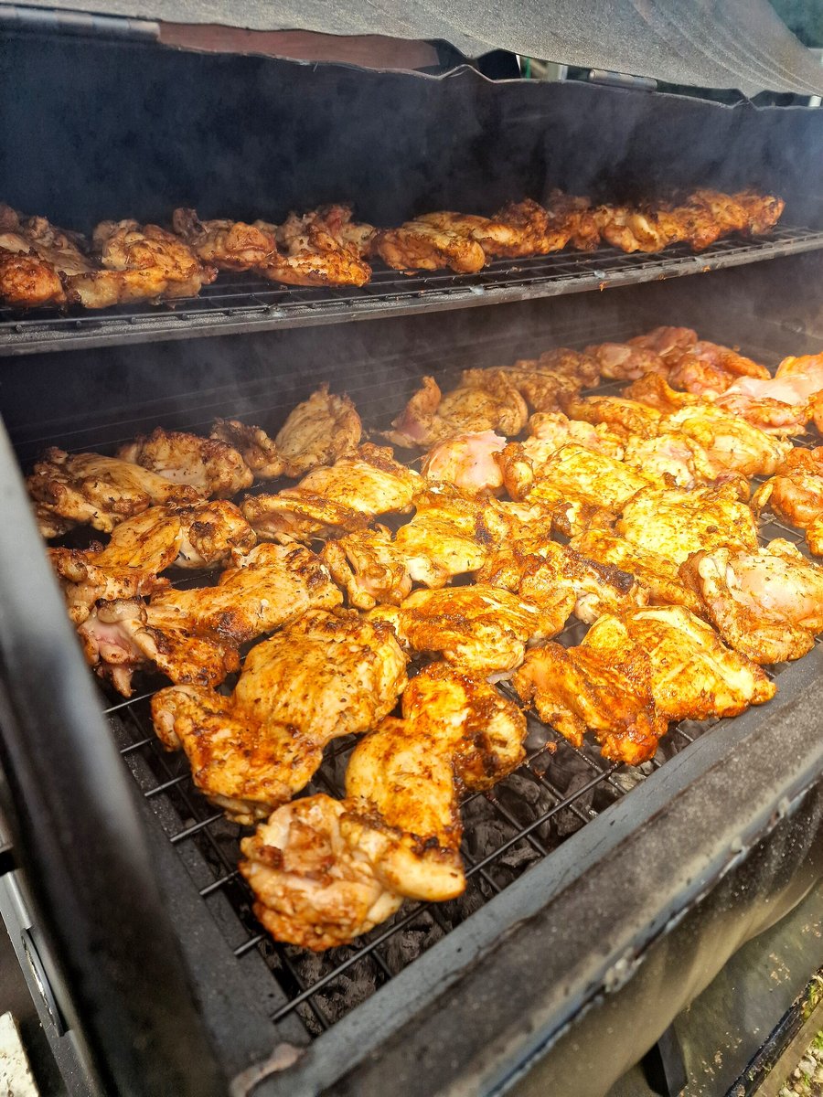 Chicken pieces are grilling on a large smoker with visible smoke