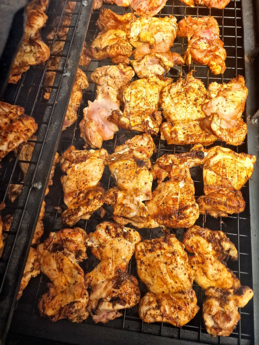 Marinated chicken thighs cooking on a barbecue grill with visible char marks