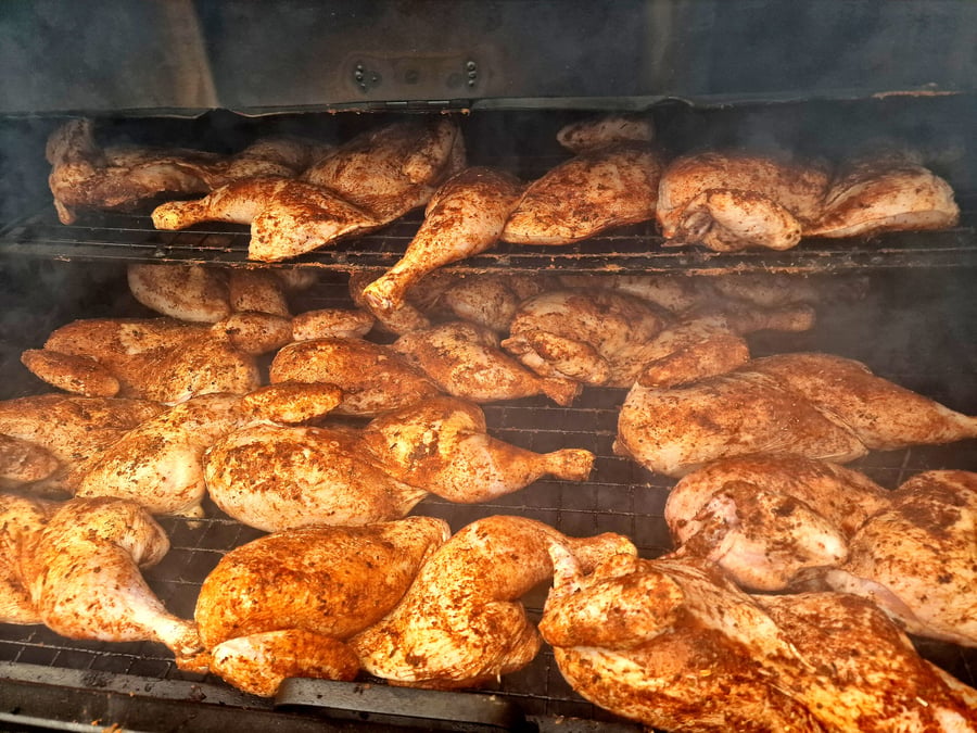 Many seasoned chickens are smoking and cooking on multiple racks inside a smoker