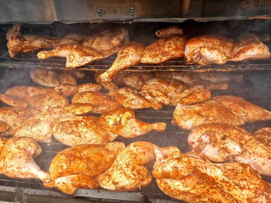 Many seasoned chickens are smoking on multiple racks inside a large smoker