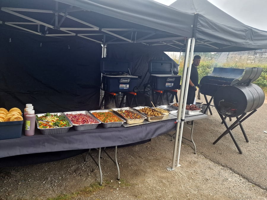 Outdoor catering setup with a buffet spread and a large barbecue grill
