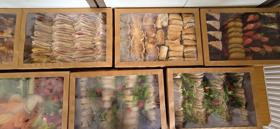 Assortment of catering boxes filled with sandwiches, pastries, cake, and fruit