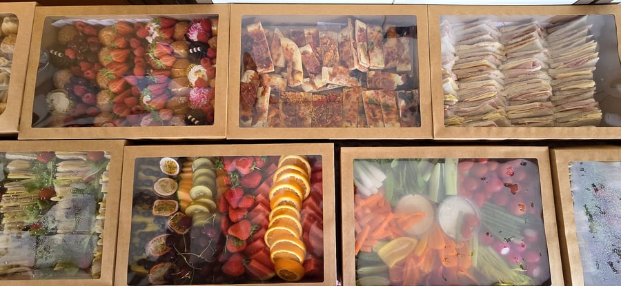 Assortment of catering boxes filled with sandwiches, fruit, pizza, pastries, and vegetables