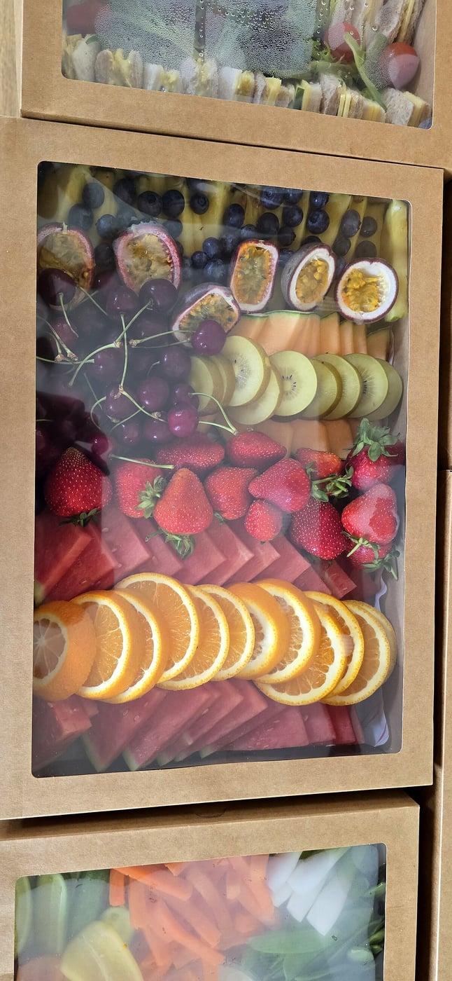 A beautifully arranged fruit platter in a catering box, featuring fresh strawberries, oranges, and watermelon