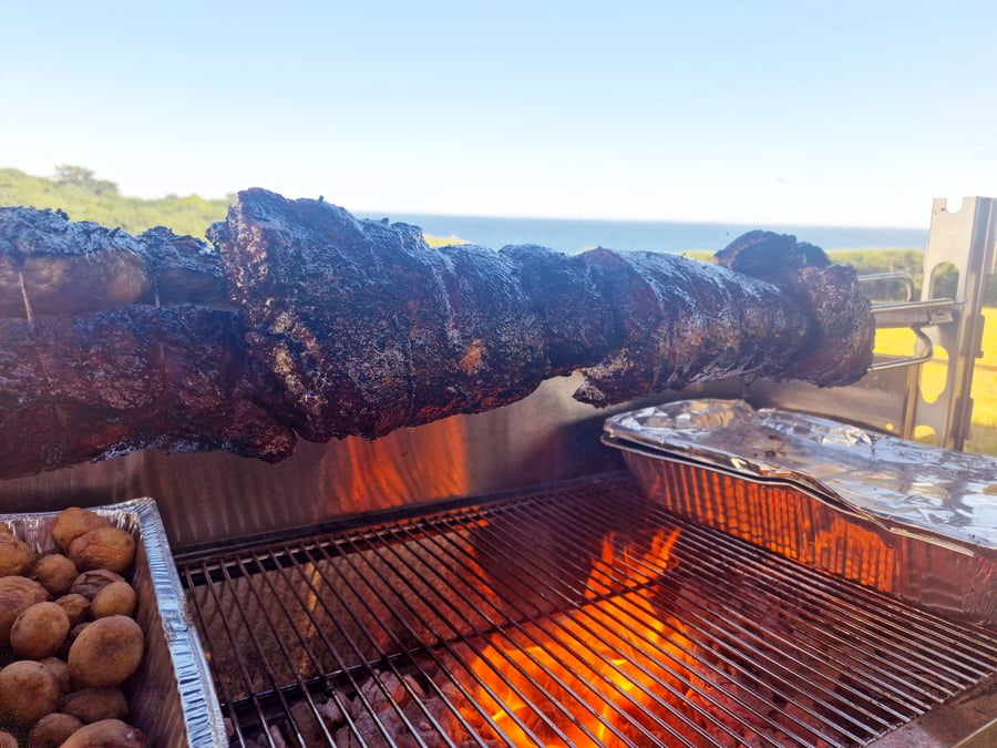 A large piece of meat is roasting on a spit over an open fire outdoors