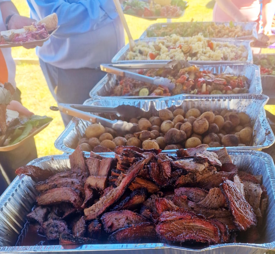 Trays of delicious BBQ meats and salads are laid out for an outdoor event