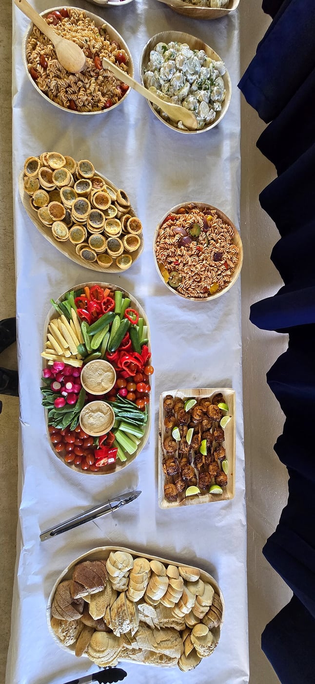 A long table displays a variety of buffet dishes including salads, bread, and skewers