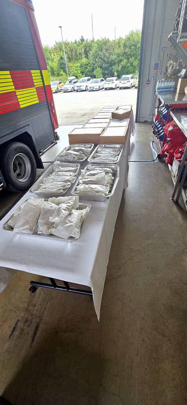 Catering trays of food laid out on a table next to a fire engine