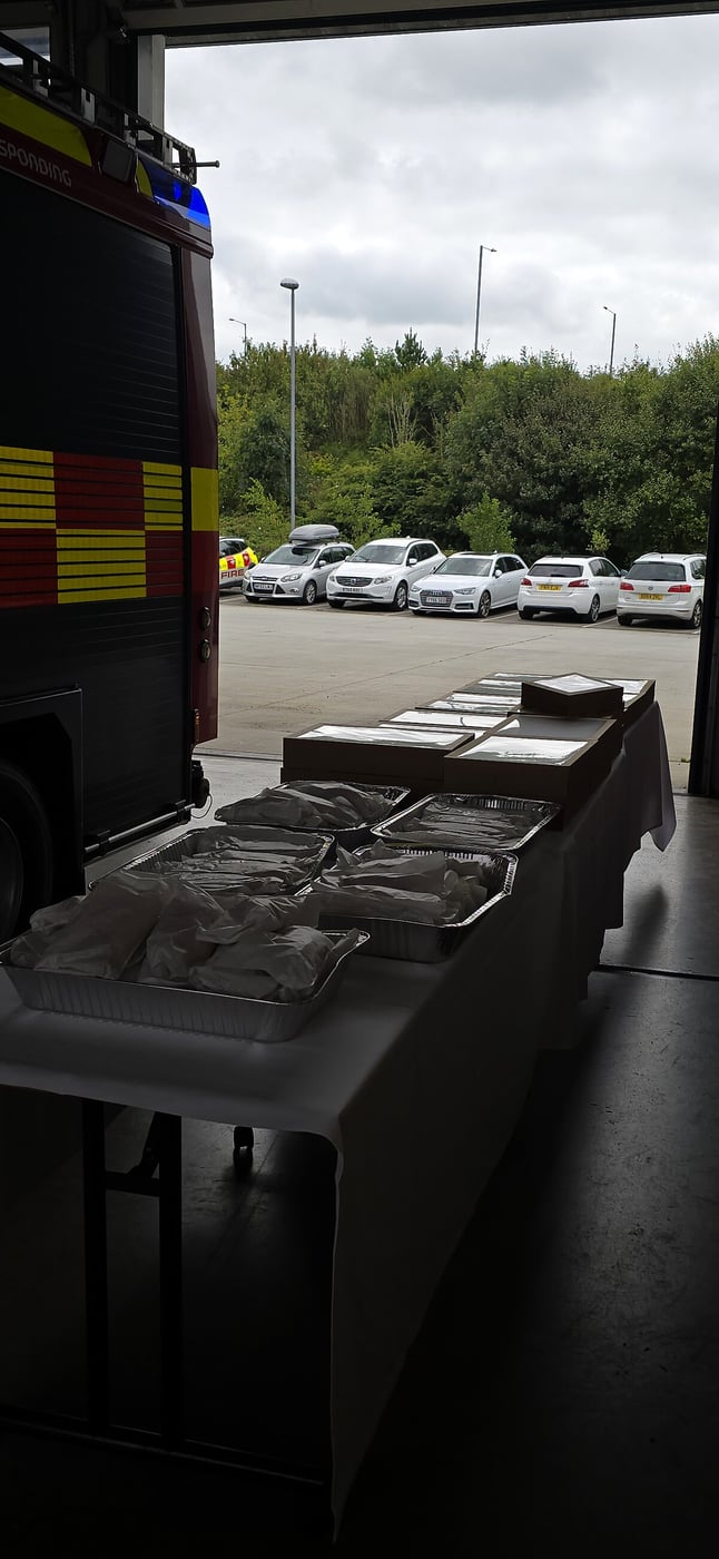 Catering trays of food are laid out on tables in front of a fire engine