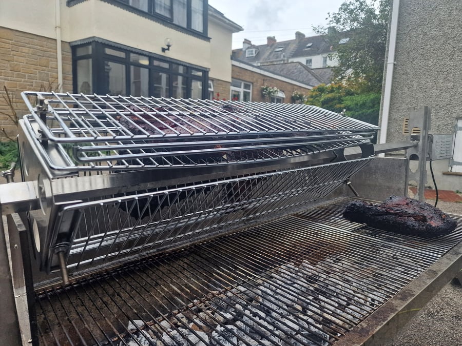 Large cuts of meat are slow-cooking on a rotisserie grill over hot coals