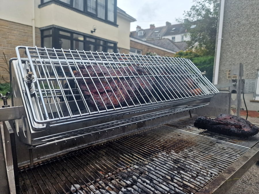 Two large cuts of brisket cooking on a professional barbecue grill outdoors