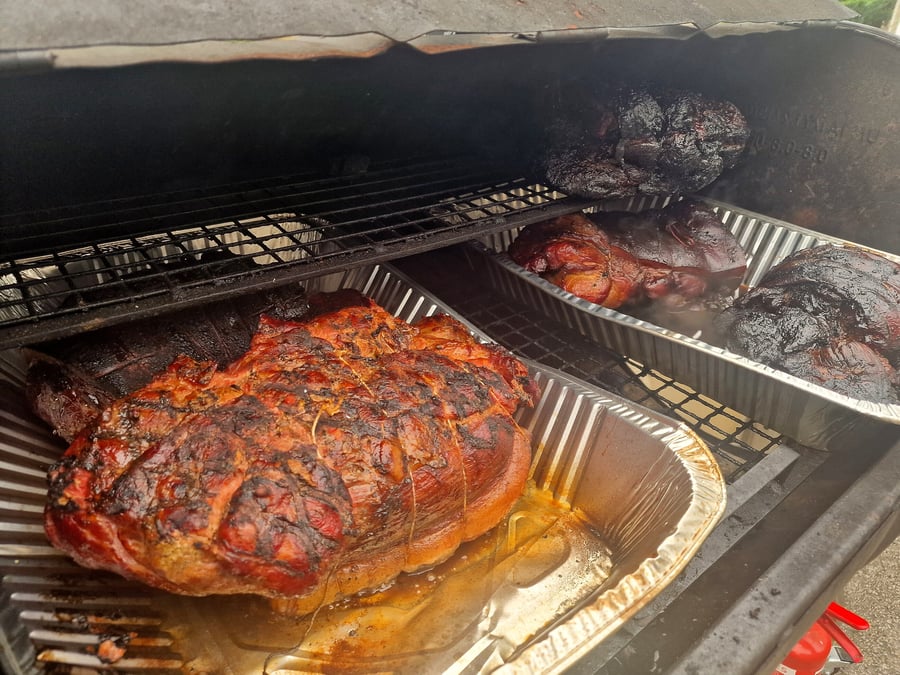 Several large cuts of pork are slow-roasting in a smoker, ready for an event