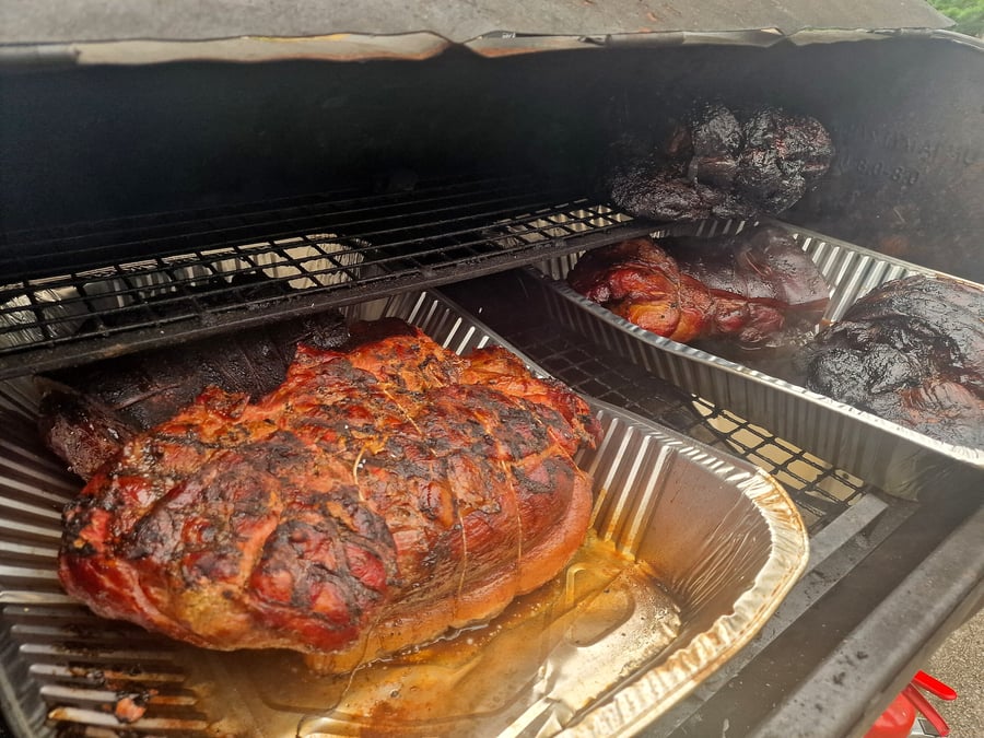 Several large pork roasts are cooking on racks inside a smoker