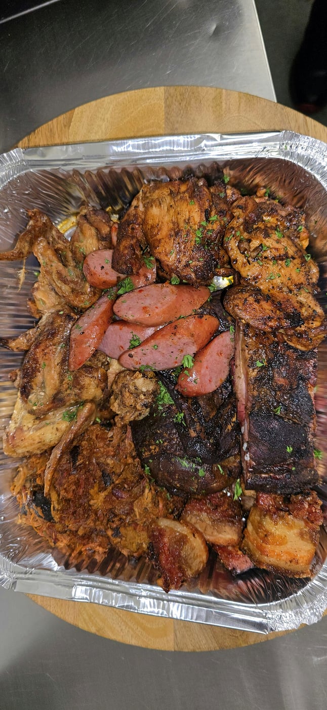 A large foil tray filled with a variety of grilled meats and sausages