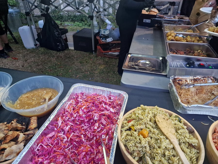 Outdoor buffet spread with various salads, pasta, potatoes, and meats under a tent