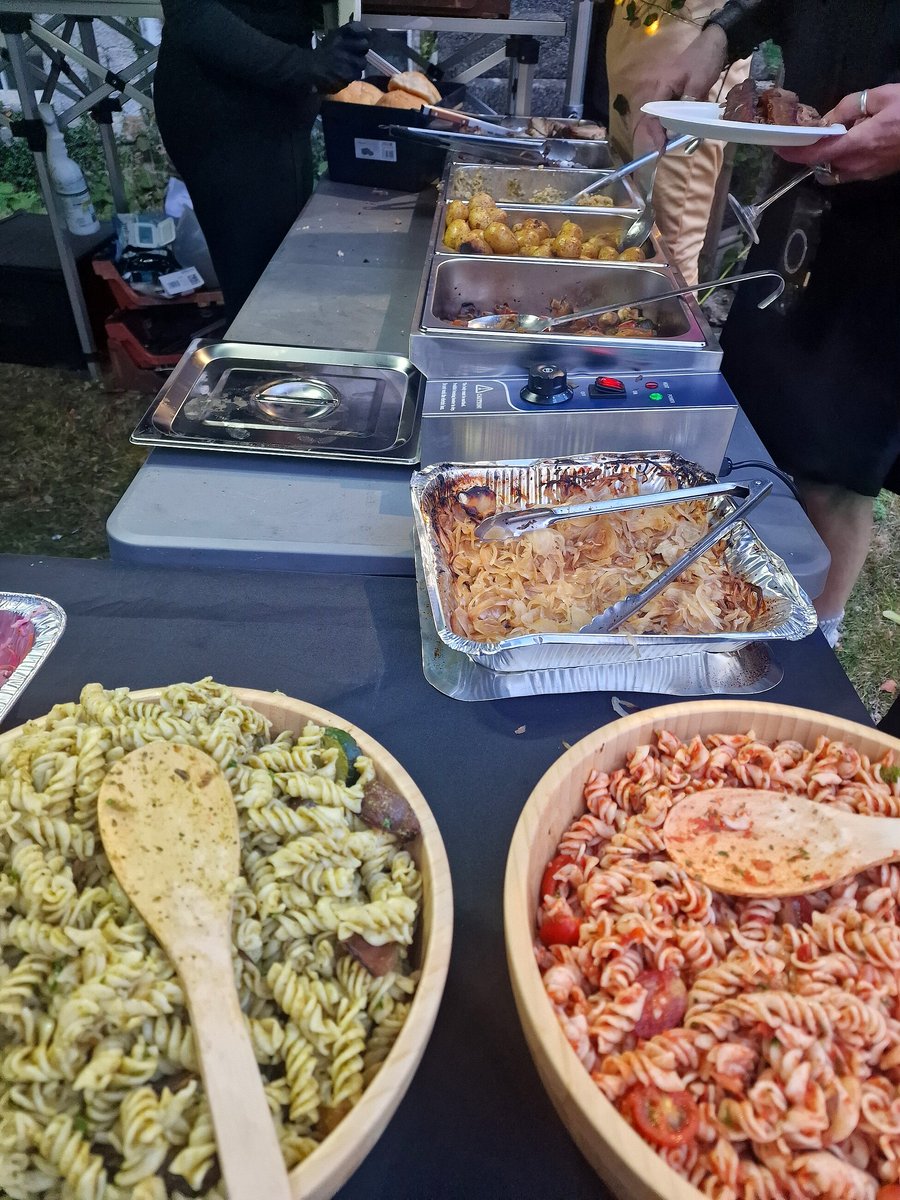 A buffet spread featuring pasta salads and hot dishes served outdoors