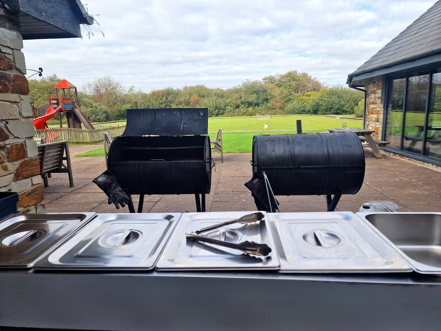 Two large barrel smokers stand ready on a patio with serving trays in the foreground