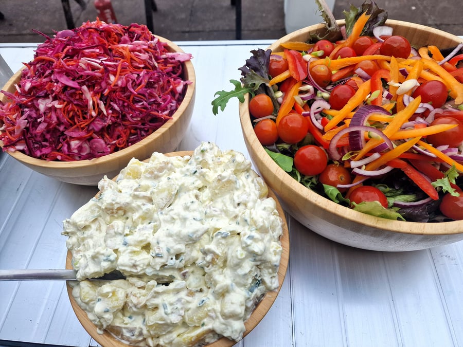 Three wooden bowls filled with fresh salads and coleslaw, ready for serving