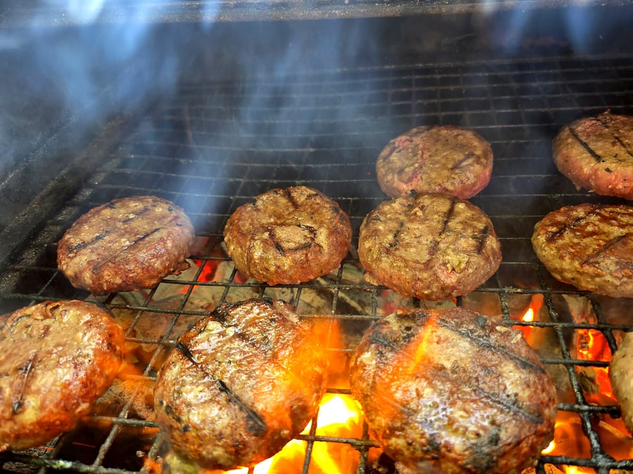 Juicy burgers are grilling over hot coals with visible smoke and flames