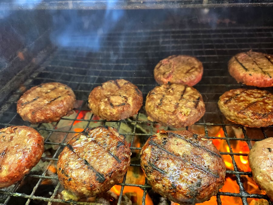 Juicy burgers are grilling over hot coals with visible smoke and flames (2)
