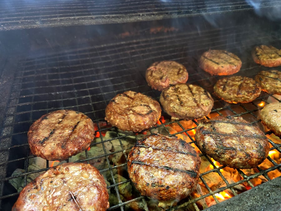 Juicy burgers are sizzling and grilling over hot coals with visible smoke