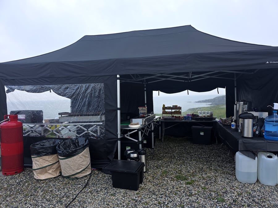 Outdoor catering setup under a black tent with a coastal view