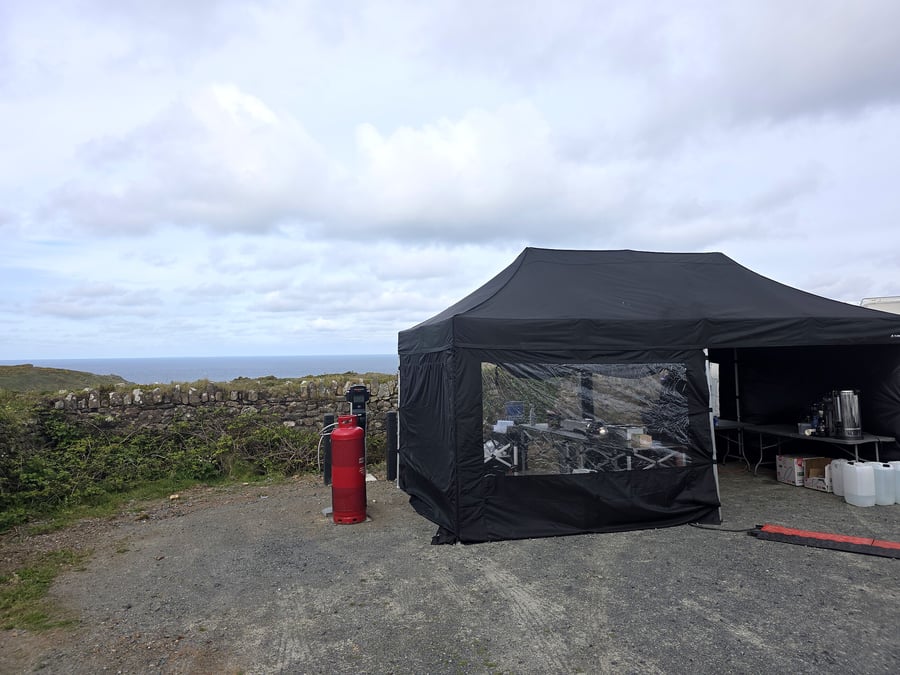 A black catering tent is set up outdoors with a gas cylinder and equipment