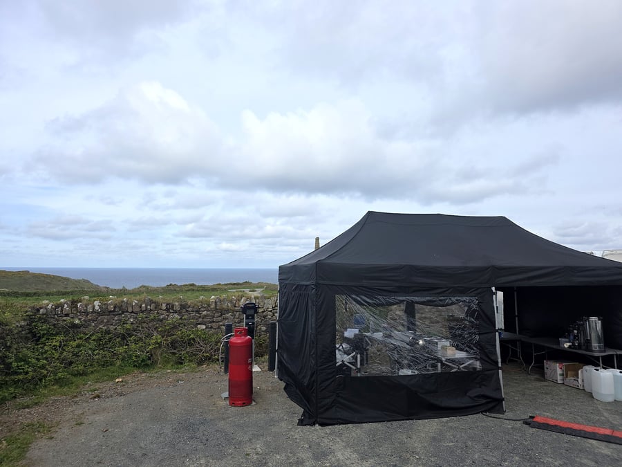 A black catering tent is set up outdoors with a coastal view and gas bottle