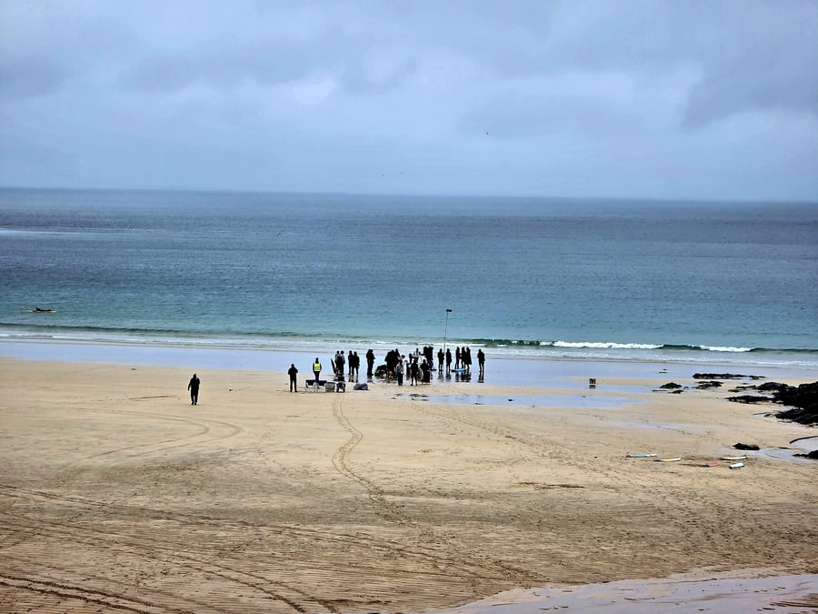 Film crew gathered on a beach with the ocean and cloudy sky