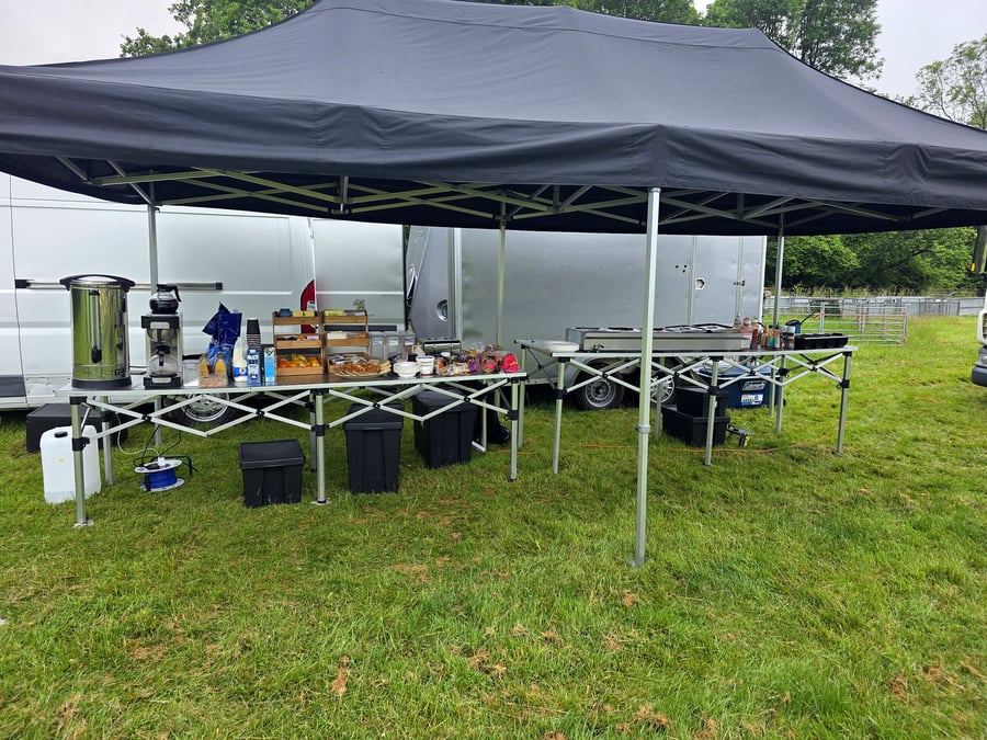 Outdoor catering setup with a tent, tables, food, and drinks