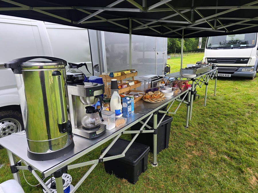 Outdoor catering setup with coffee, pastries, and drinks under a tent