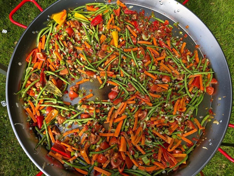 A giant paella pan filled with fresh, colourful vegetables ready for cooking