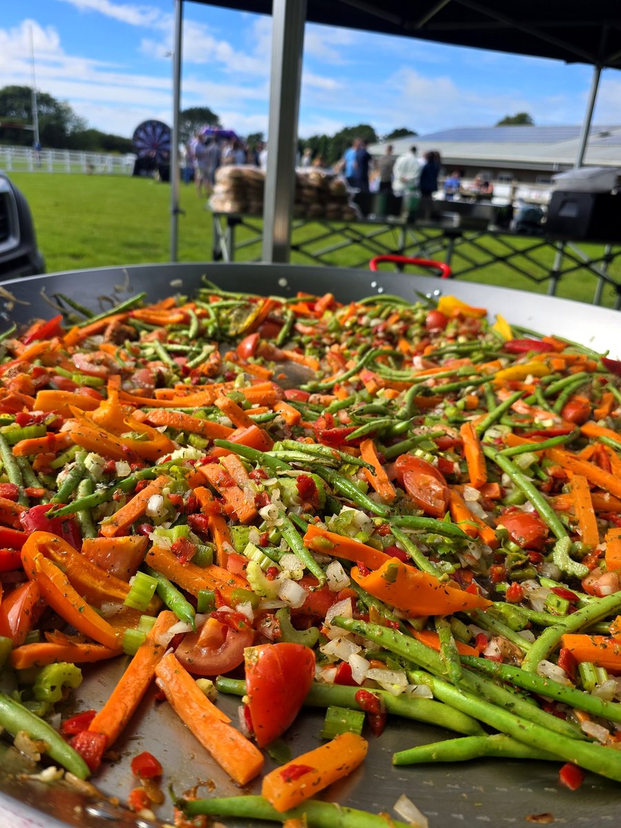 A giant pan filled with colourful vegetables, ready to be served at an outdoor event
