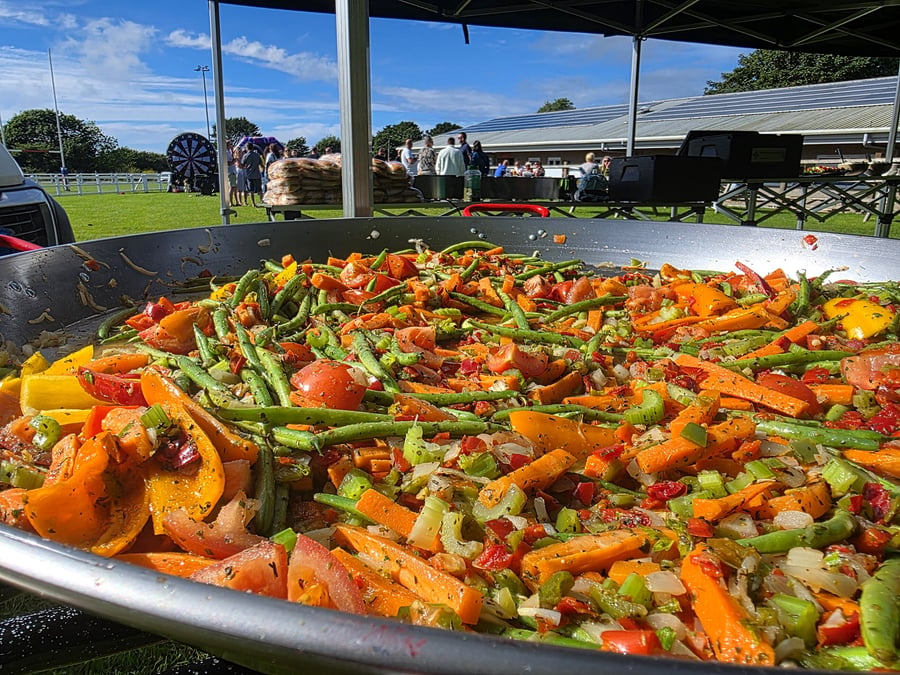 A giant pan filled with colourful, fresh vegetables prepared for an outdoor event